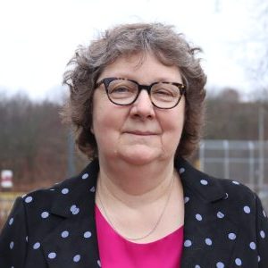 Photo of Karen. A woman with short, curly hair. She is wearing glasses.