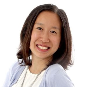 Photo of Aiann. A young woman smiling, she has shoulder length hair and is wearing a purple sweater.