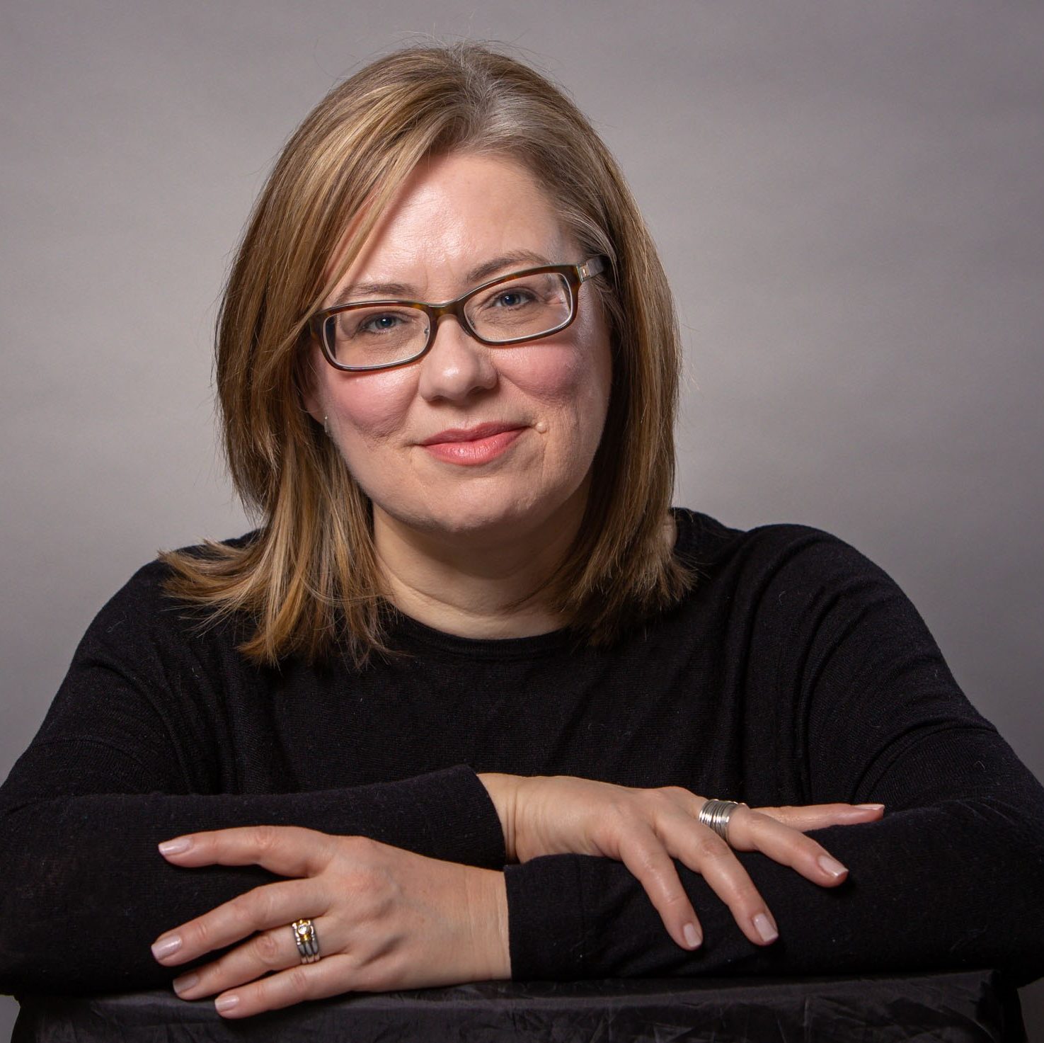 Photo of Jennifer. A woman with blonde hair wearing black glasses with thick lenses.
